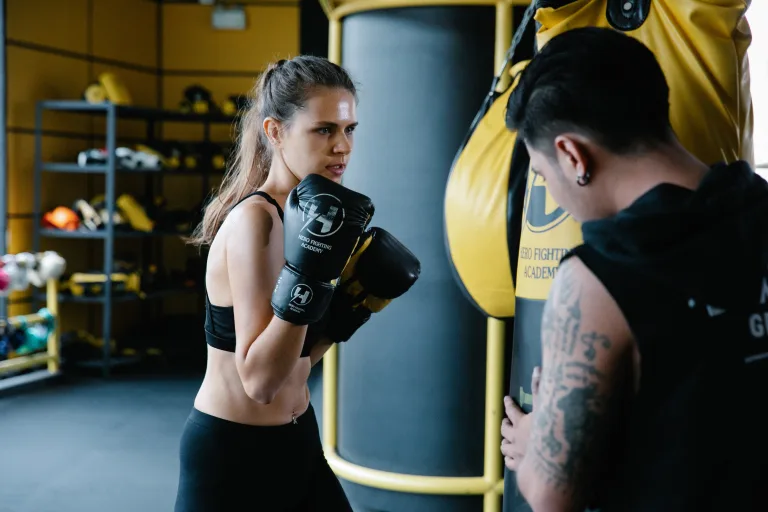 Focused woman wearing black tank tops practicing boxing with trainer high intensity interval training