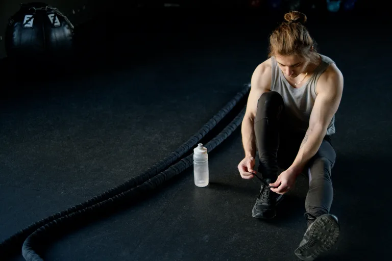 man tying shoes beside good temperature bottled water and battle ropes