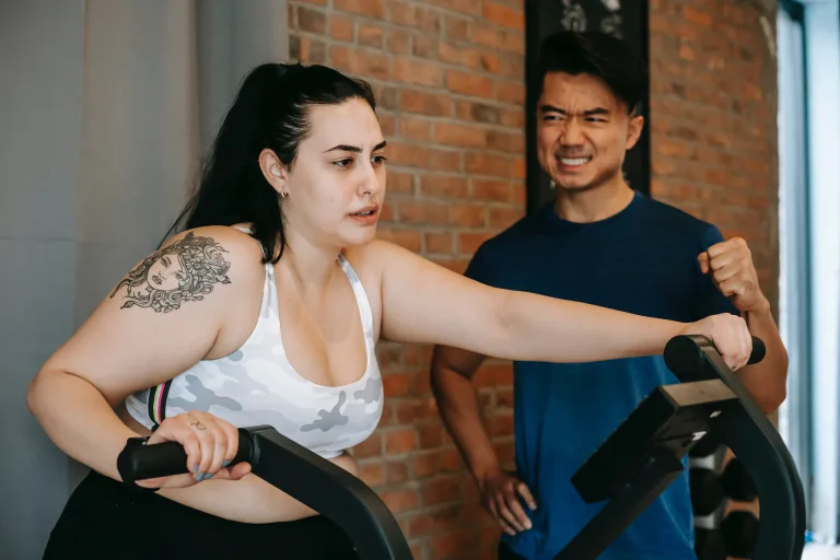 A trainer is motivating a woman while doing exercise on gym equipment to overcome obesity