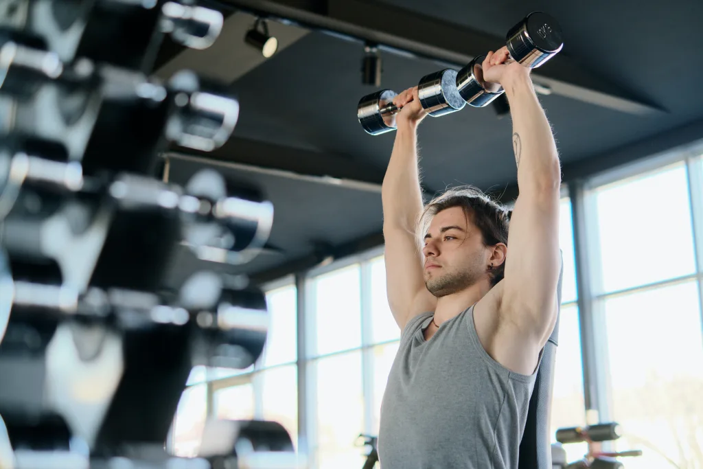 serious man wearing gray tank tops lifting dumbbells in the gym weight loss