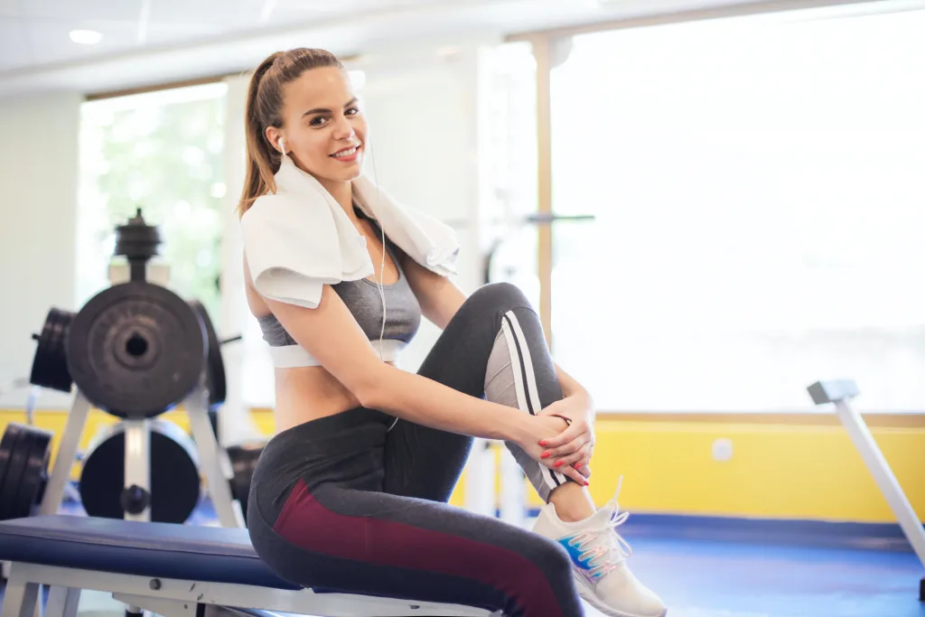 smiling woman resting on gym equipment after exercise before water intake active recovery