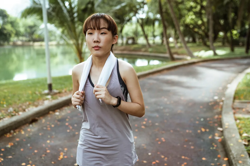 Asian woman with towel above her shoulder jogging on an empty park-weight loss