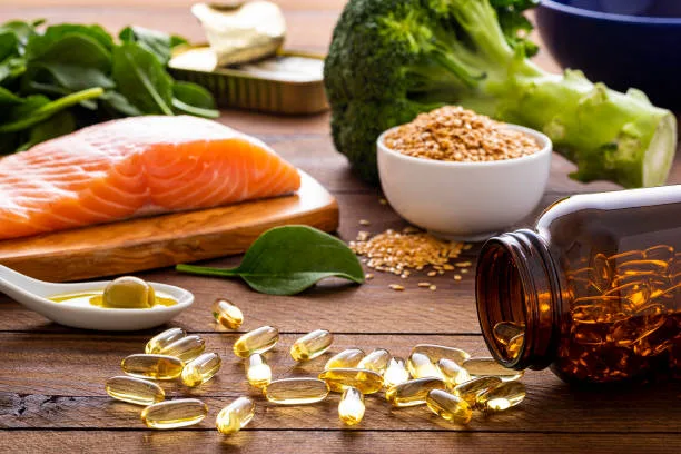 Front view of many fish oil capsules spilling out from the bottle surrounded by an assortment of food rich in omega-3 such as salmon, flax seeds, broccoli, sardines, spinach, olives and olive oil. good for weight loss